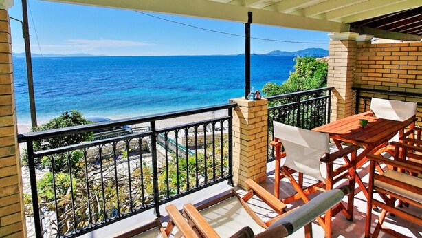Un balcón con vista al mar, un muro de ladrillo y una mesa de madera con sillas.