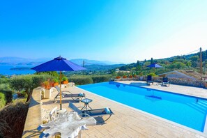 Une piscine entourée de chaises longues et de parasols, bordée de murs en pierre et agrémentée de plantes en pot, offrant une vue imprenable sur un paysage pittoresque.