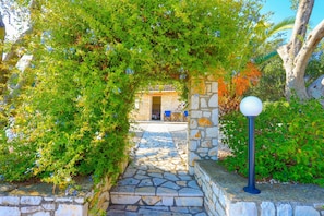 Guests enter through a charming stone pathway surrounded by lush greenery and plants.