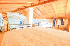 Cozy attic retreat with a large bed, stone wall, and ceiling fan.