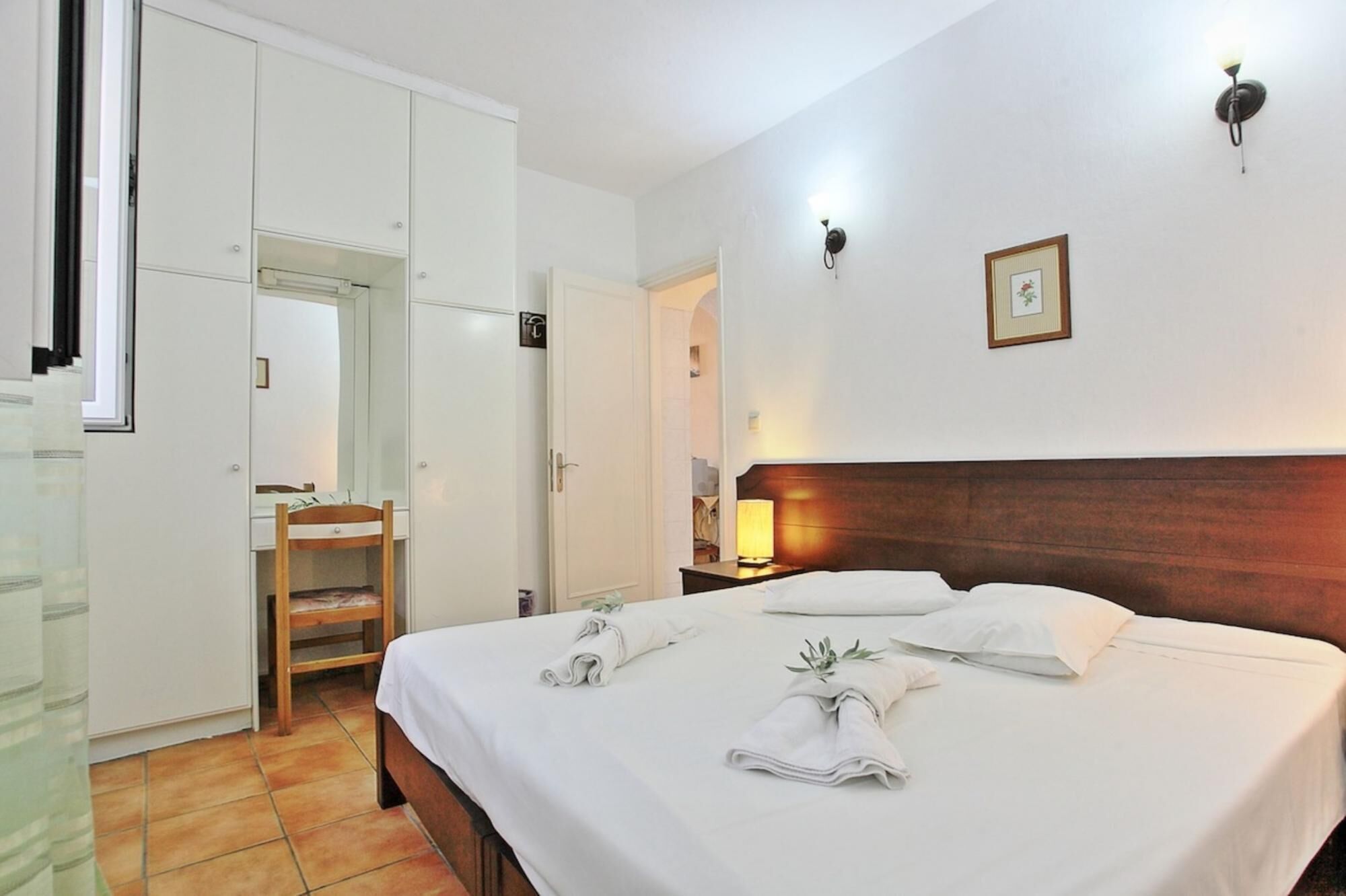 A hotel room with a bed, a wardrobe, a mirror, and a nightstand with a lamp.