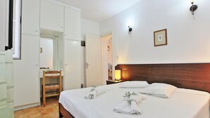 A hotel room with a bed, a wardrobe, a mirror, and a nightstand with a lamp. - Dina Beach Front Apartment (Corfu)