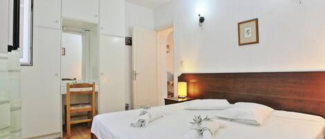 A hotel room with a bed, a wardrobe, a mirror, and a nightstand with a lamp.