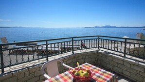 A balcony with a checkered tablecloth, a bottle, and a basket of fruit. - Dina Beach Front Apartment (Corfu)