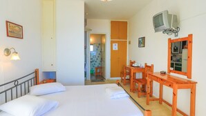 A hotel room with a bed, a desk, a chair, a television, and a bathroom visible through an open door. - Faros Tessera in Gaios (Paxos)