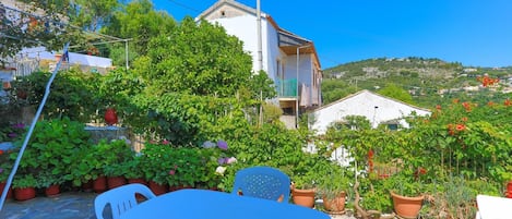 A patio with a table and chairs, surrounded by potted plants and a white building with a balcony.