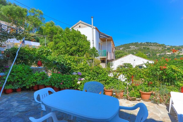 Eine Terrasse mit Tisch und Stühlen, umgeben von Kübelpflanzen und einem weißen Gebäude mit Balkon.