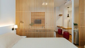 Ein modernes Schlafzimmer mit einem Bett, einer Holzwand, einem kleinen Tisch mit Lampe und einem roten Hocker.