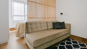 Ein modernes Wohnzimmer mit einem beigefarbenen Sofa, einem gemusterten Teppich und einem Raumteiler aus Holzlamellen.