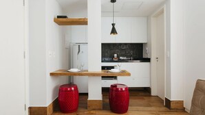 Eine kompakte Küche mit weißen Schränken, einer Holz Arbeitsplatte und einer schwarzen Spritzschutzwand. Zwei rote Hocker und eine Pendelleuchte sind vorhanden.