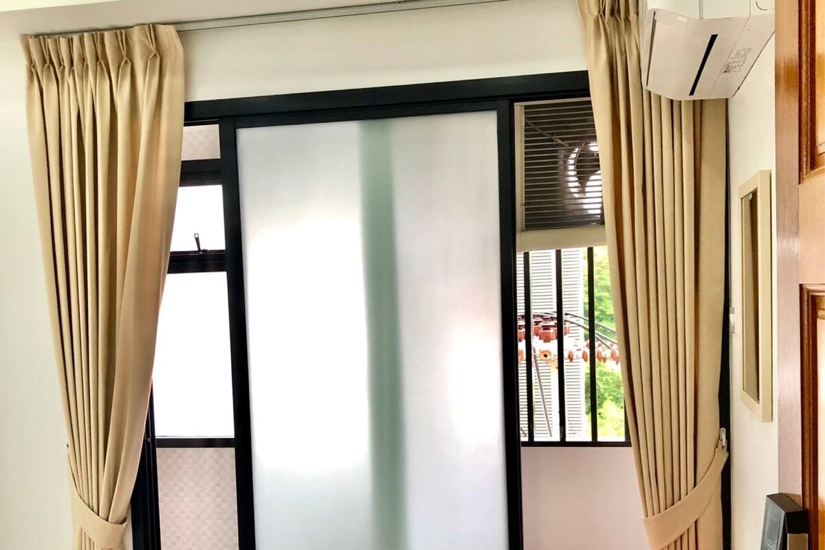A hotel room with a bed, a wooden table with a coffee maker, and a sliding glass door leading to a balcony.