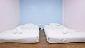 A room with two single beds against a blue wall, a wooden floor, and a small table with a chair. - Orange Hotel Kuala Pilah (Kuala Pilah)