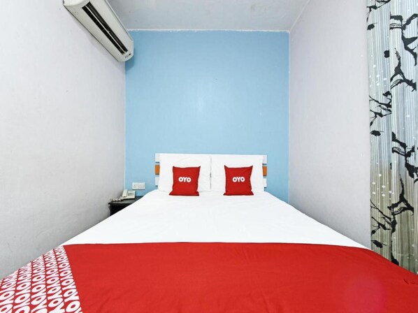 A hotel room with a bed, two red pillows with "OYO" branding, a white bedspread, and a patterned curtain.