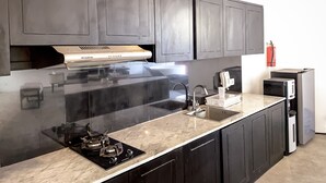 Una cocina moderna con armarios oscuros, una campana extractora de acero inoxidable, una estufa a gas, un fregadero y un microondas.