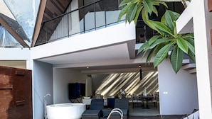 Un área de piscina moderna al aire libre, con jacuzzi, asientos y vista al espacio interior.