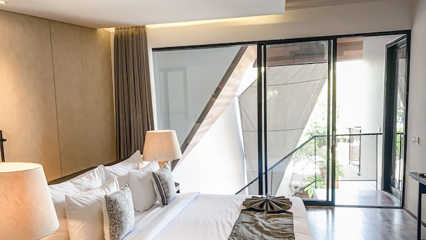 Habitación de hotel moderna con una cama grande, dos lámparas de noche, vistas al balcón exterior y una puerta corrediza de vidrio que da al balcón.