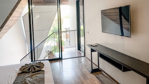 Un interior moderno con un amplio ventanal corredera que da a un balcón, un televisor montado en la pared y un mueble consola minimalista.