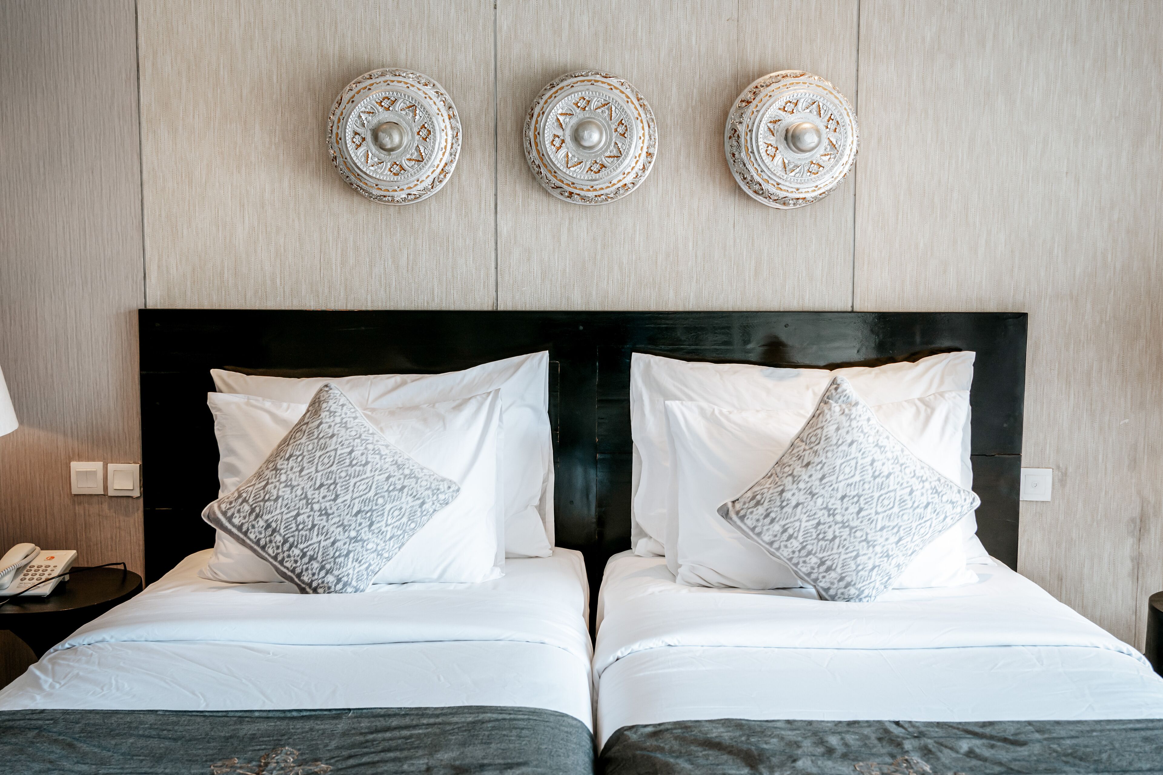 A double bed with white linens and patterned pillows, a black headboard, and decorative wall plates.