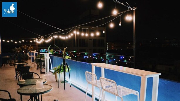 An outdoor seating area with tables and chairs, string lights, and a blue railing. - By Dee @Jomtien (Pattaya)