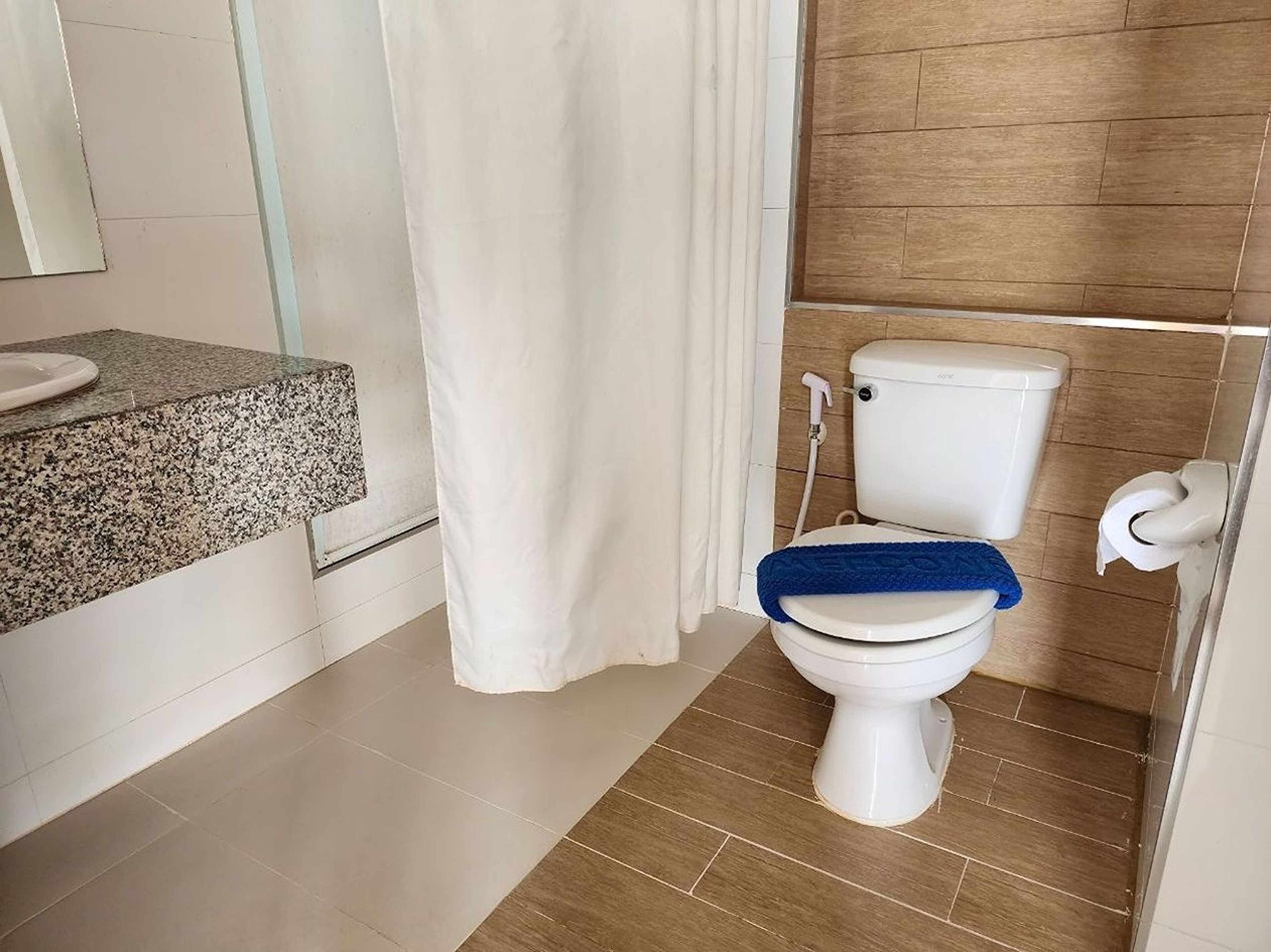 Een badkamer met een wit toilet, een douchegordijn en een wastafel op een granieten blad.