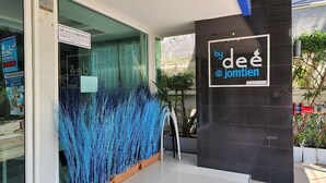 A modern building entrance with a glass door, a sign reading "by deé @ jomtien", and a decorative blue plant arrangement. - By Dee @Jomtien (Pattaya)