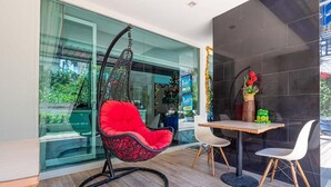 A modern interior with a glass wall, a hanging chair, a dining table, and chairs. - By Dee @Jomtien (Pattaya)