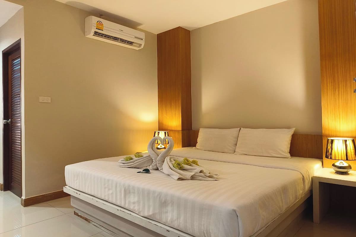 Een hotelkamer met een bed, een nachtkastje, een wandairconditioner en een deur met houten frame.
