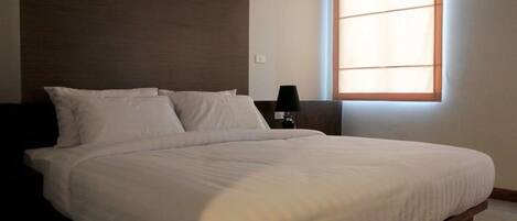 A large bed with a wooden headboard, a nightstand with a lamp, and a window with blinds.