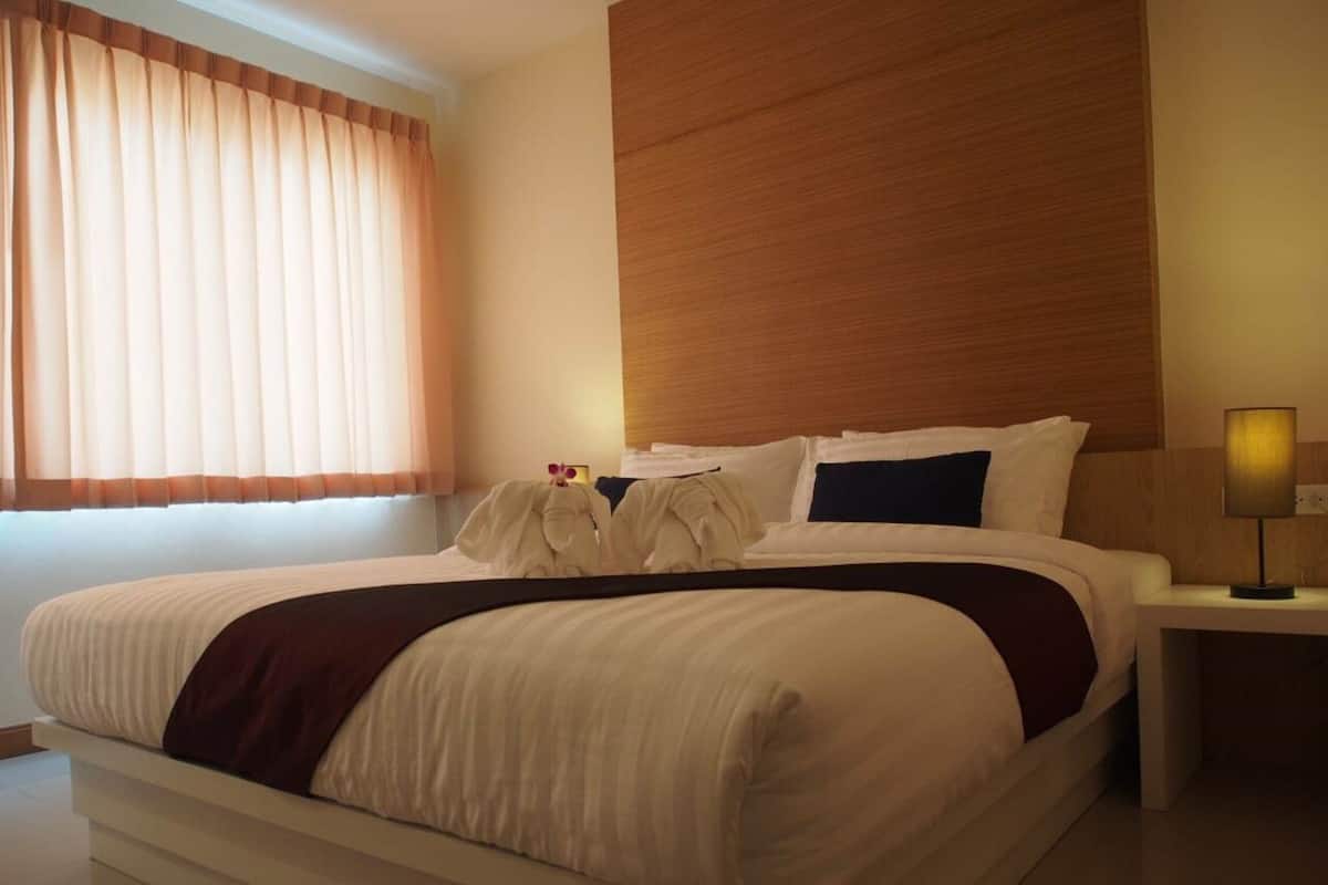 Een moderne hotelkamer met een groot bed, een houten hoofdbord, een nachtkastje met een lamp en een raam met gordijnen.