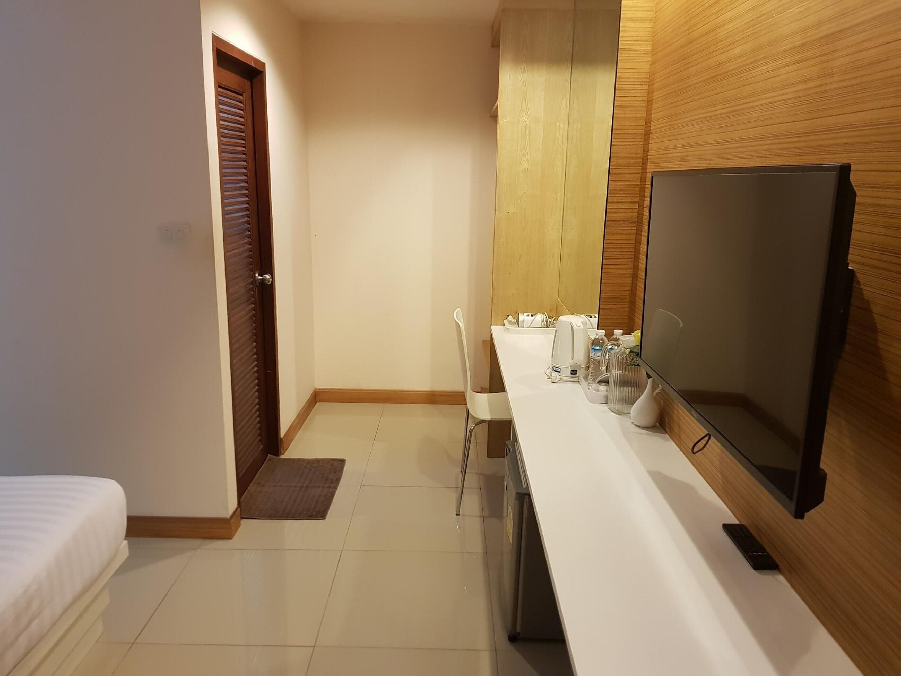 A hotel room with a bed, a desk with a TV, a chair, and a small kitchenette area.