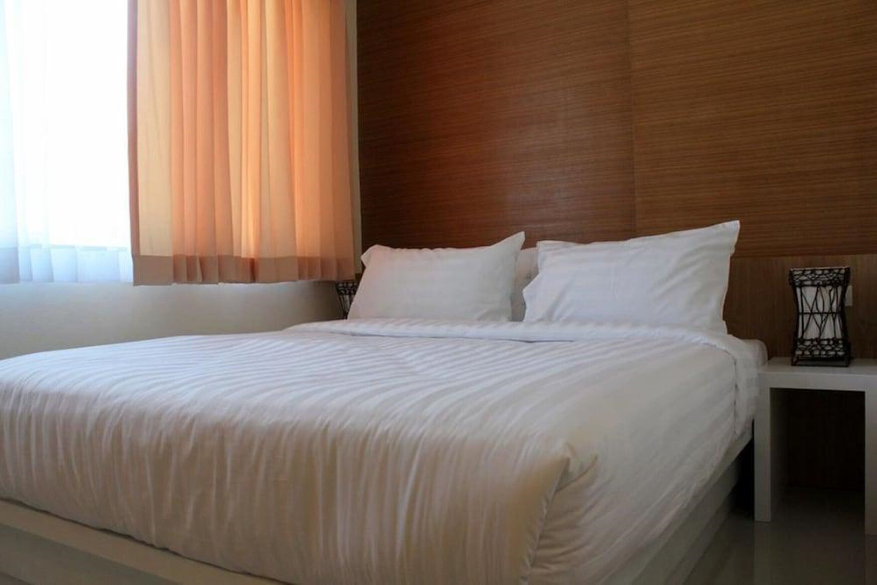 A neatly made bed with white linens in a modern room with wooden paneling and a nightstand with a lamp.