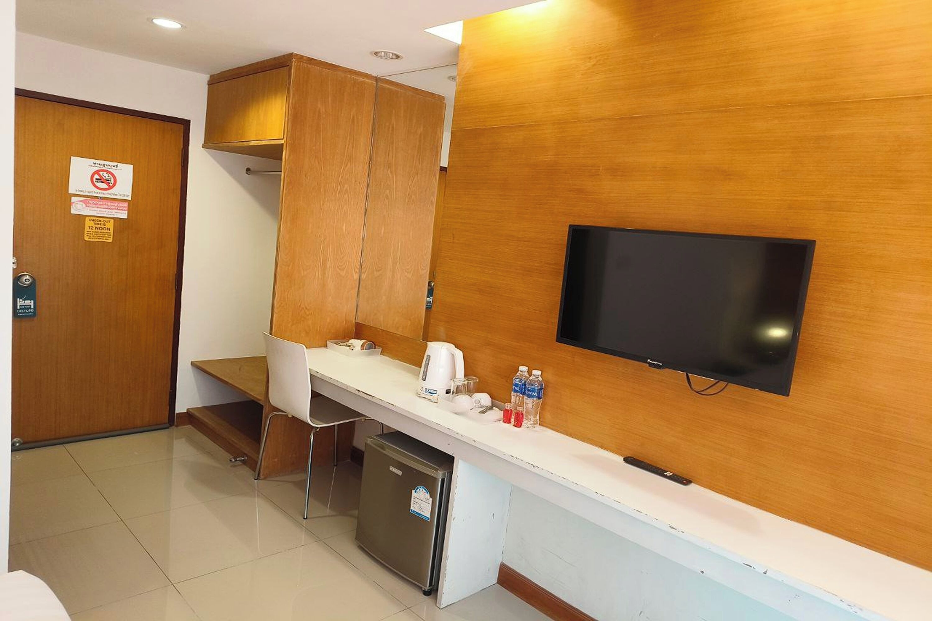 A hotel reception area with a wooden counter, a television mounted on the wall, a refrigerator, and a sign indicating no smoking.