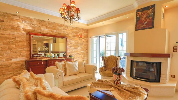 A spacious living room with a stone wall, a fireplace, a chandelier, and a large window. - Eleonas in Kato Korakiana (Corfu)