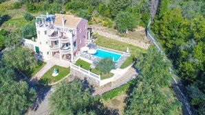A large, multi-story building with a swimming pool, surrounded by lush greenery and a stone wall. - Eleonas in Kato Korakiana (Corfu)