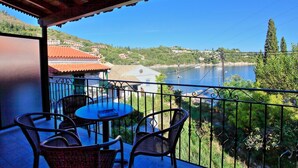 Ein Balkon mit Tisch und Stühlen mit Blick auf einen See, umgeben von Grünflächen und Gebäuden.