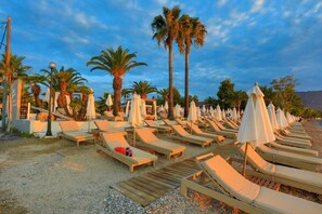 A beachside resort with rows of sun loungers and umbrellas, palm trees, and a clear sky. - Senses Suite Dio in Dassia (Corfu)