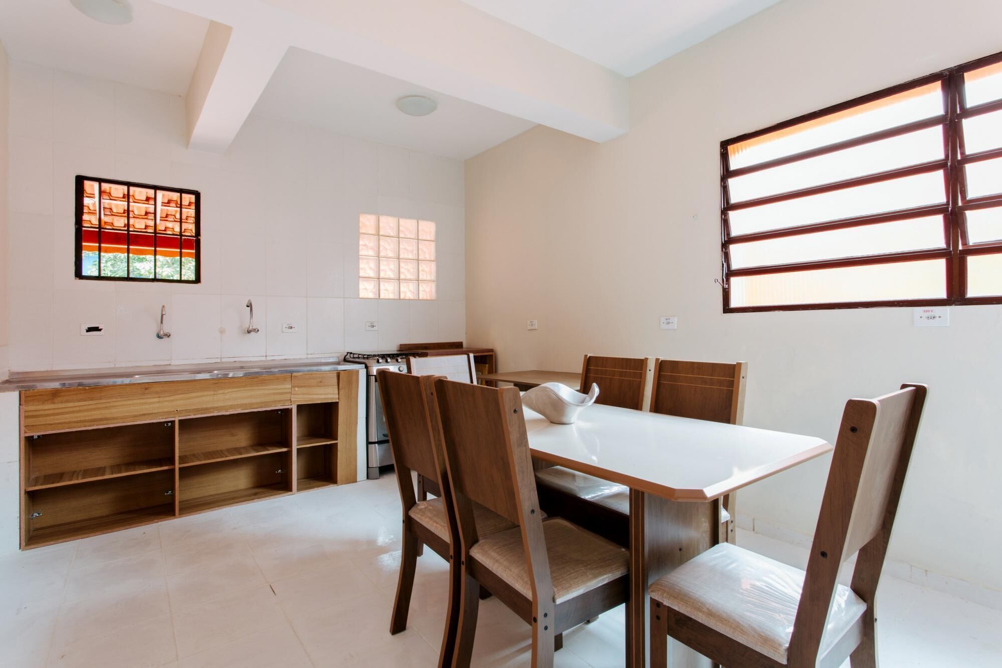 A modern kitchen with white cabinets, a wooden countertop, and a built-in oven. There is a dining table with four chairs and a window with blinds.