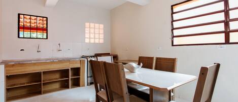 A modern kitchen with white cabinets, a wooden countertop, and a built-in oven. There is a dining table with four chairs and a window with blinds.