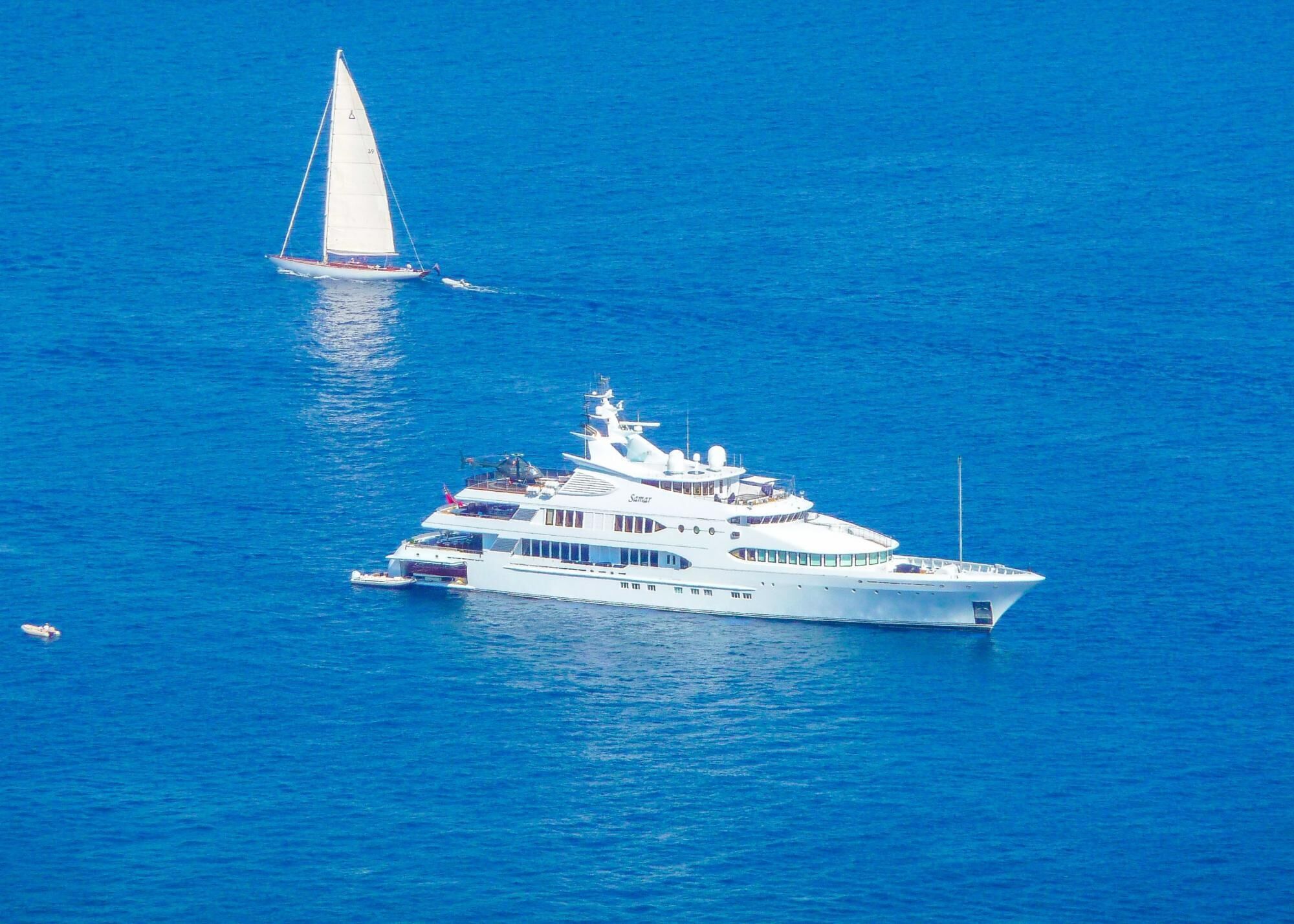 A large white yacht with multiple decks and a helipad, sailing in the ocean.