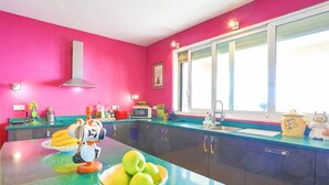 A kitchen with a pink wall, a window, and a bowl of green apples on the counter. - Villa Triantafyllo in Kentroma (Corfu)