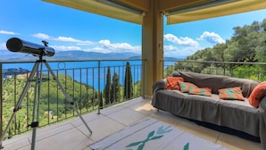 A balcony with a telescope, a sofa with cushions, and a view of a lake and mountains. - Villa Triantafyllo in Kentroma (Corfu)