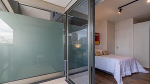 A modern bedroom with a glass door leading to a balcony, a bed with white bedding, and a city view. - Rep1203 Setin Downtown Rep Blica (São Paulo)