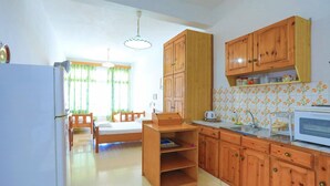 A compact kitchen with wooden cabinets, a dining table with chairs, and a refrigerator.