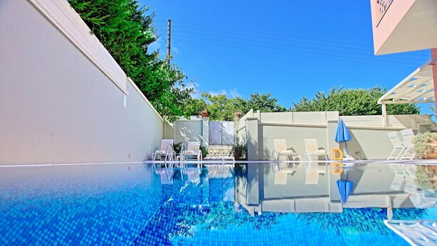 Une piscine aux eaux cristallines, bordée de chaises longues et d’ombrelles, le tout entouré d’un mur blanc et de verdure.