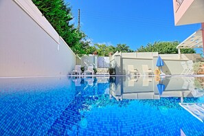 Ein klares Schwimmbecken mit Liegestühlen und Sonnenschirmen, umgeben von einer weißen Mauer und Grünpflanzen.