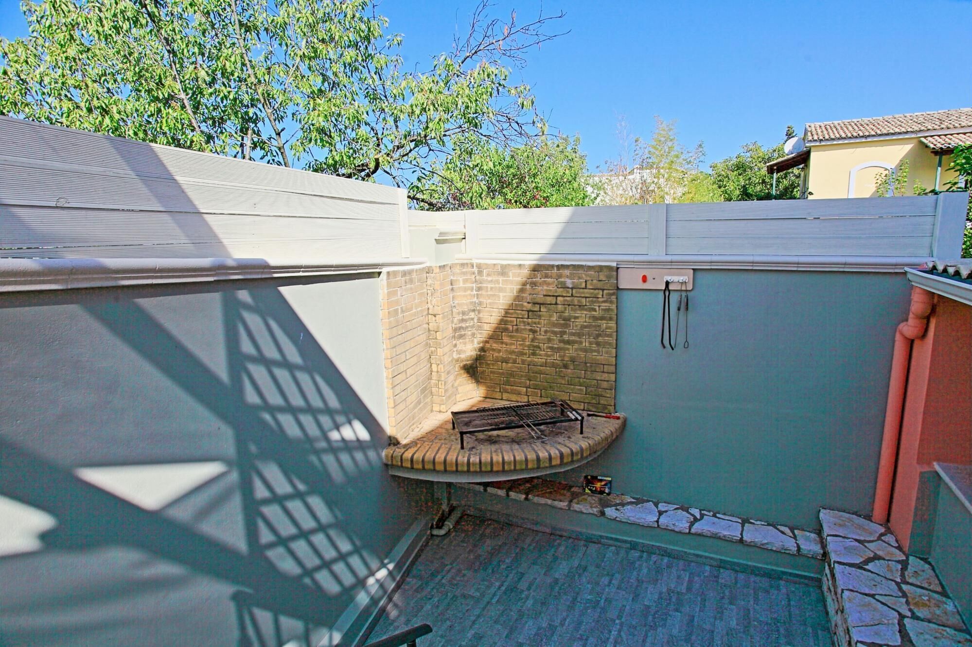 A small outdoor area with a brick wall, a metal grill, and a tiled floor.