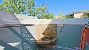 Un petit espace extérieur avec un mur en briques, un barbecue en métal et un sol carrelé.