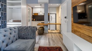 Een moderne woonkamer met een grijze bank, een houten accentmuur en een keuken op de achtergrond.