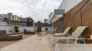 Een terras op het dak met lounge stoelen, een klein zitgedeelte en uitzicht op de stad.