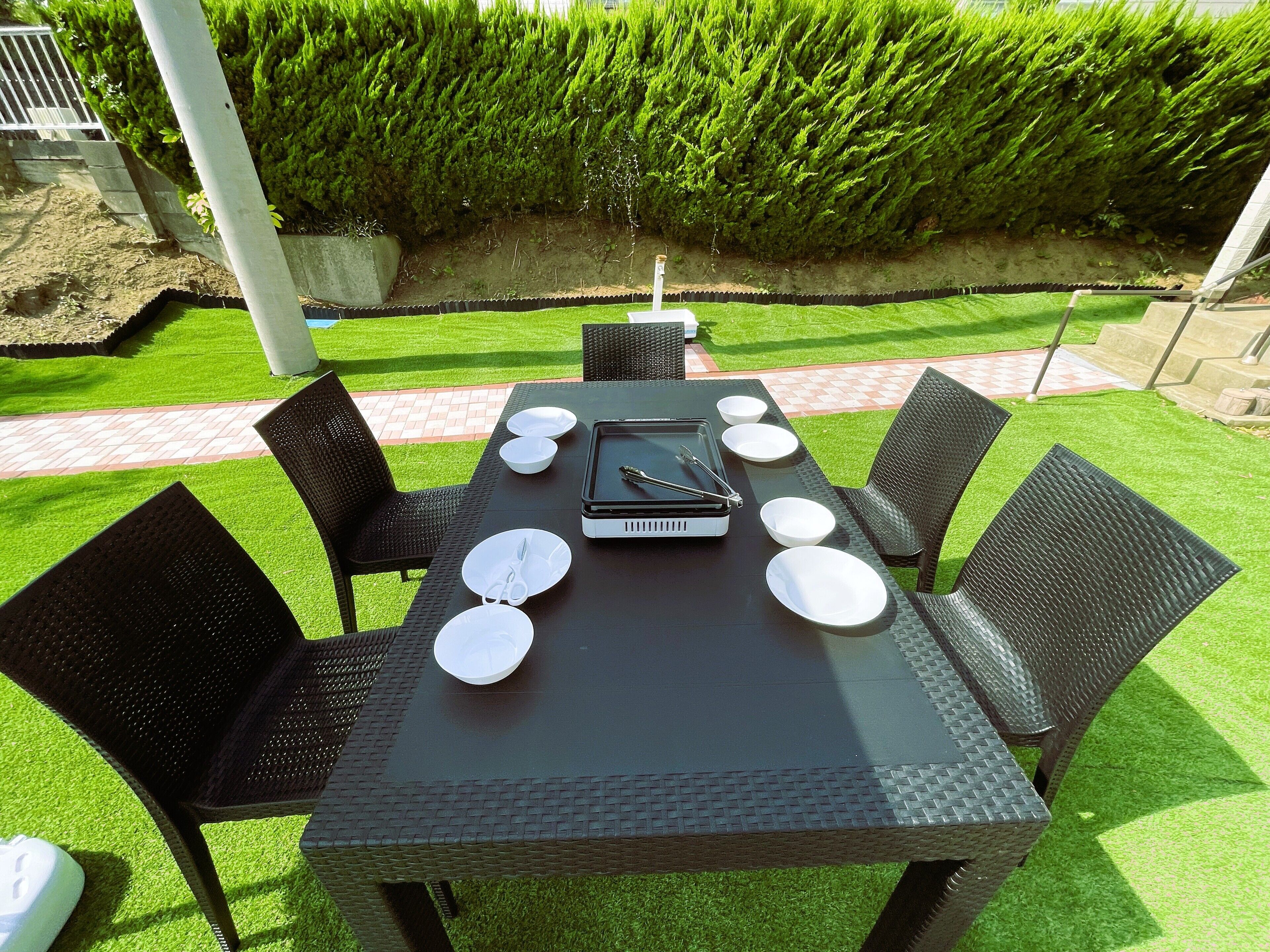 Un'area pranzo all'aperto con un tavolo apparecchiato per quattro persone, circondato da sedie e un barbecue al centro.